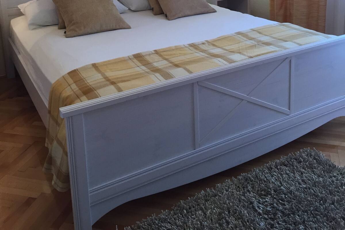 Una cama bien hecha con una manta escocesa, una lámpara de noche y un cuadro en la pared.