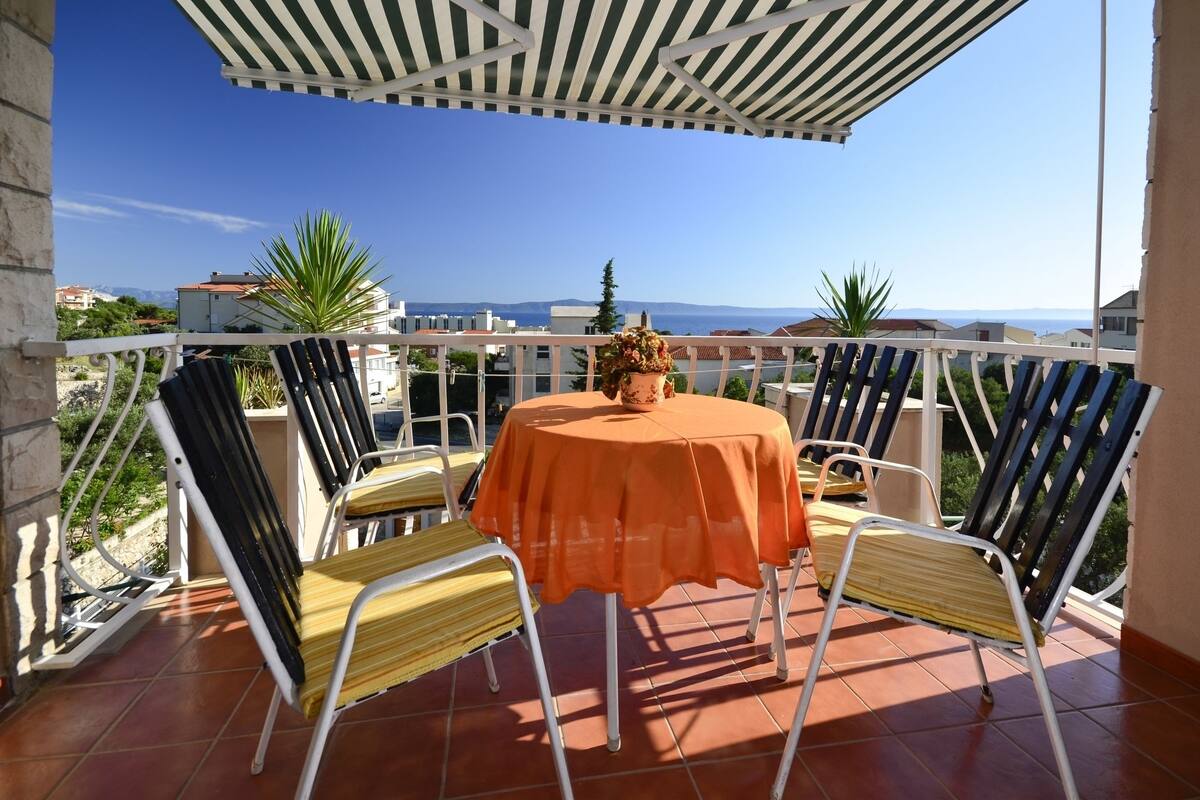 Una terraza con una mesa, sillas, una planta en maceta y vista al mar.