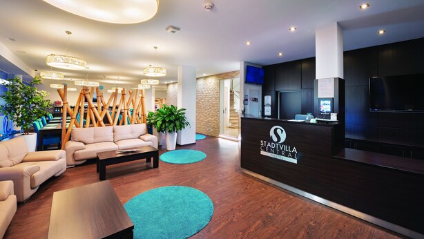 Zona de recepción de un hotel con diseño moderno, que incluye un mostrador de recepción, un área de estar con sofás y una escalera que conduce a otras plantas.