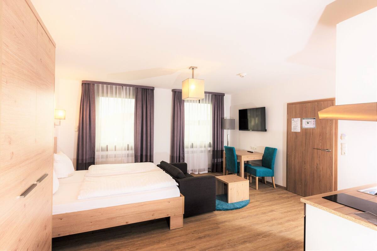 A modern hotel room with a wooden bed, a desk, a chair, and a television.