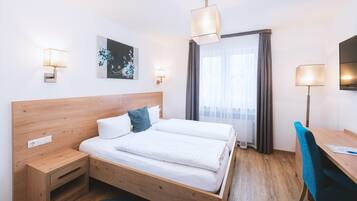 Habitación de hotel con cama de madera, escritorio y silla. Cuenta con una ventana con cortinas, un televisor montado en la pared y un cuadro.