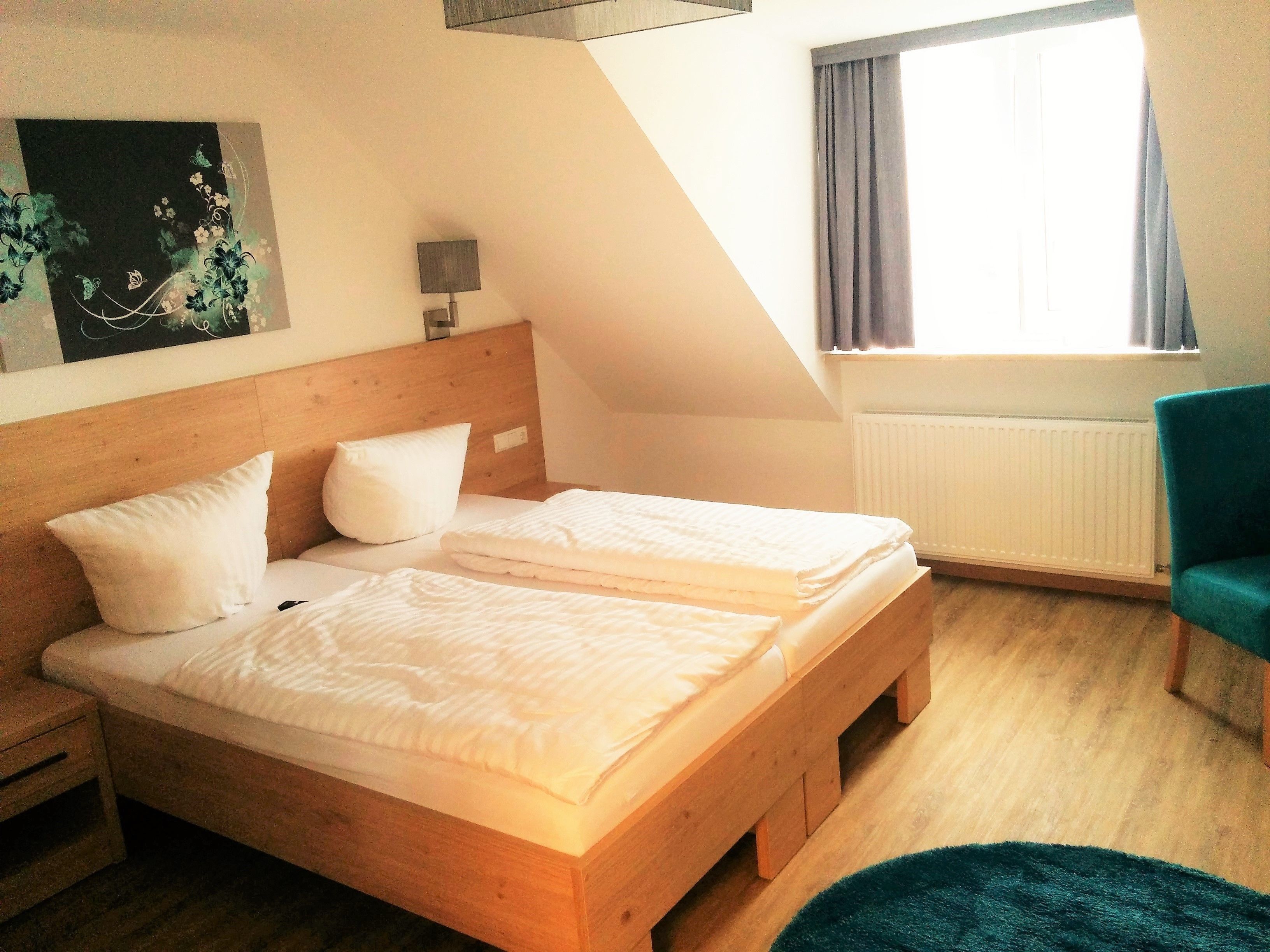 Une pièce comprenant un lit en bois, une table de chevet, une lampe, une fenêtre avec des rideaux et une chaise.