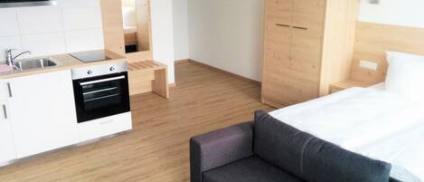 Una habitación de hotel moderna con kitchenette, un sofá, una cama y un armario de madera.