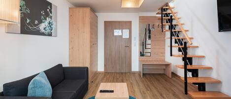 Una sala de estar moderna con un sofá, una mesa de centro, una escalera y una puerta que da a otra habitación.