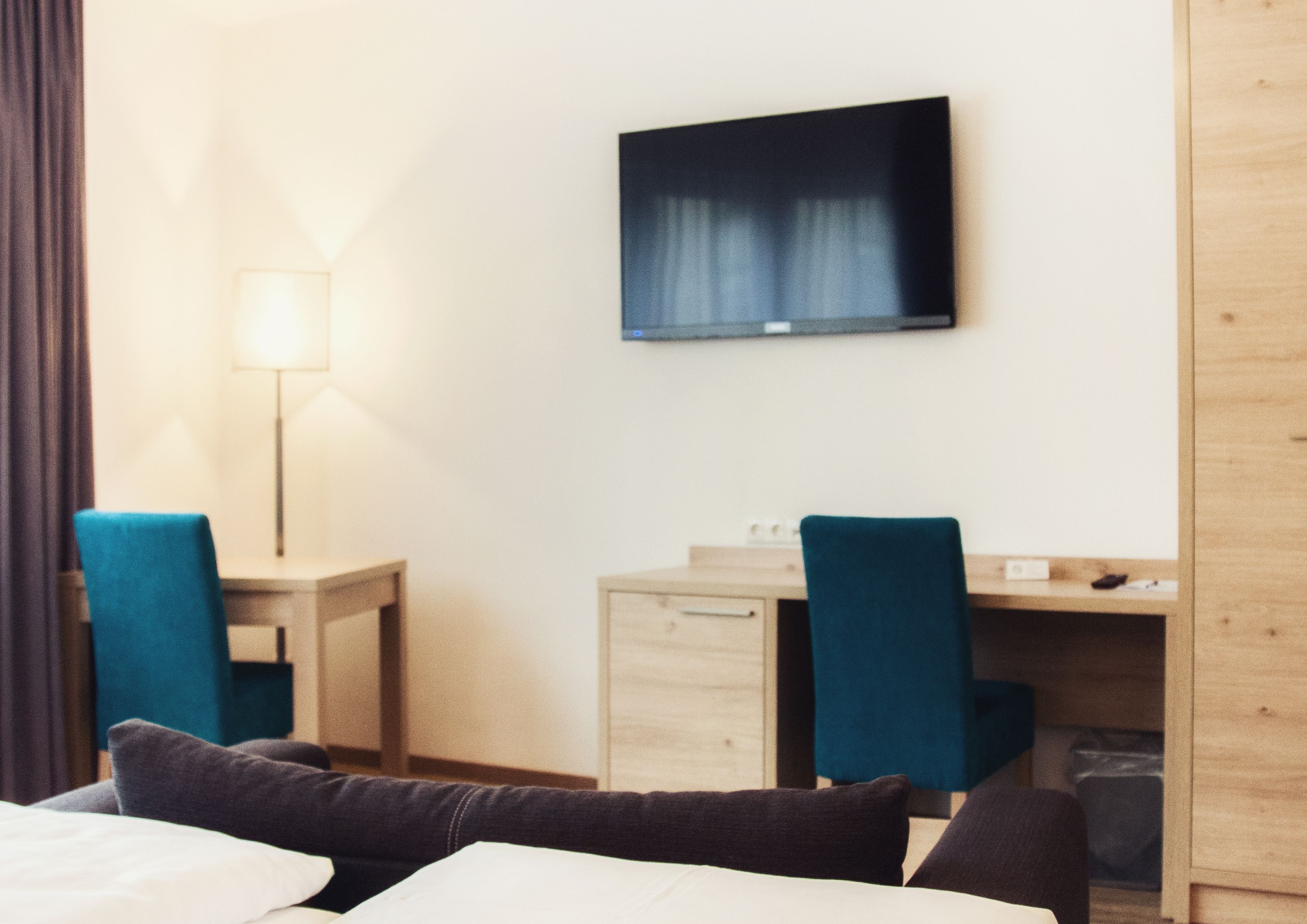 A hotel room with a bed, a desk, two chairs, a television, and a lamp.