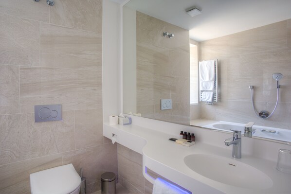 Un baño moderno con un espejo grande, un lavamanos, un inodoro y una ducha.