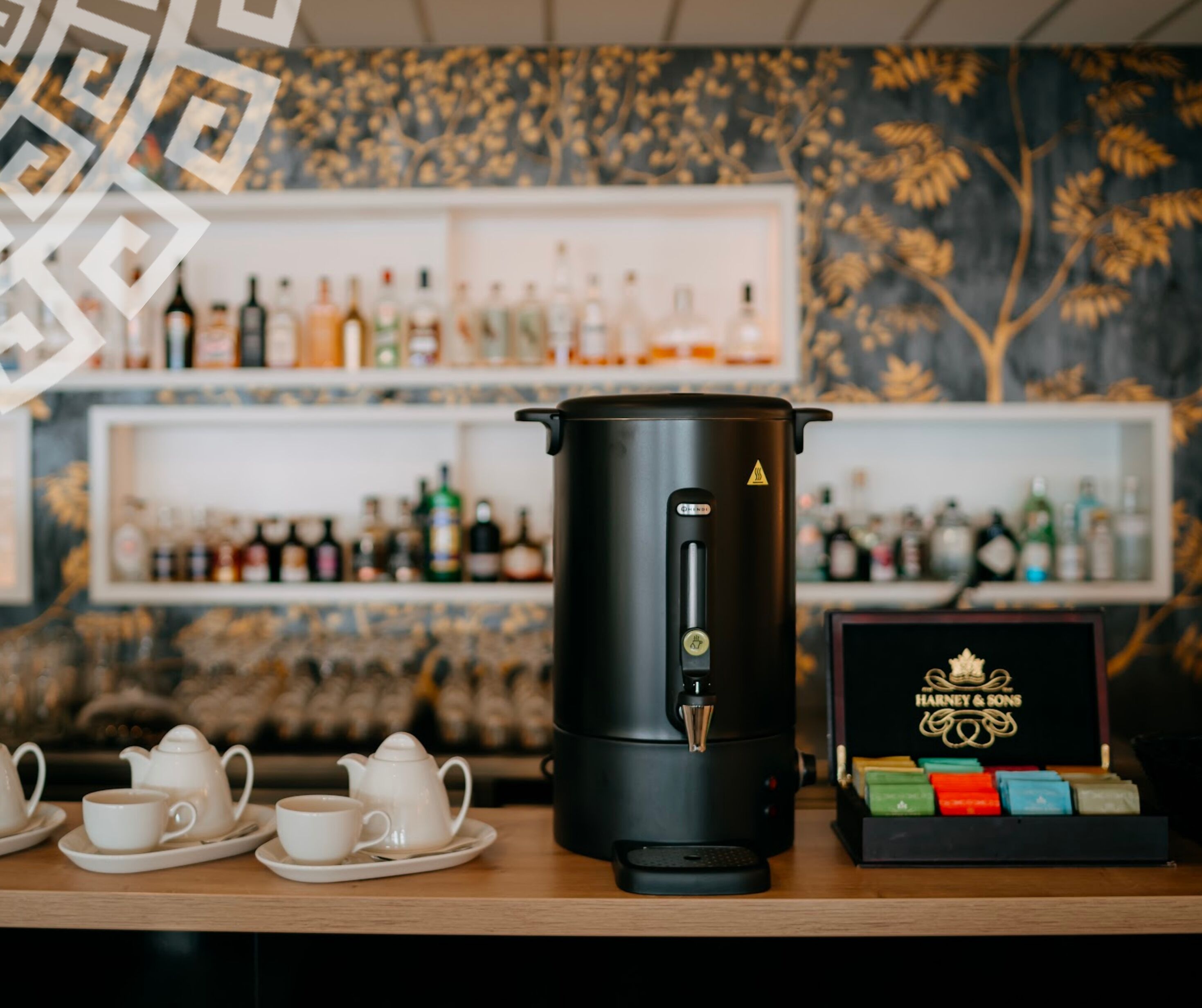 A coffee machine, teacups, and a box of tea bags on a wooden table.