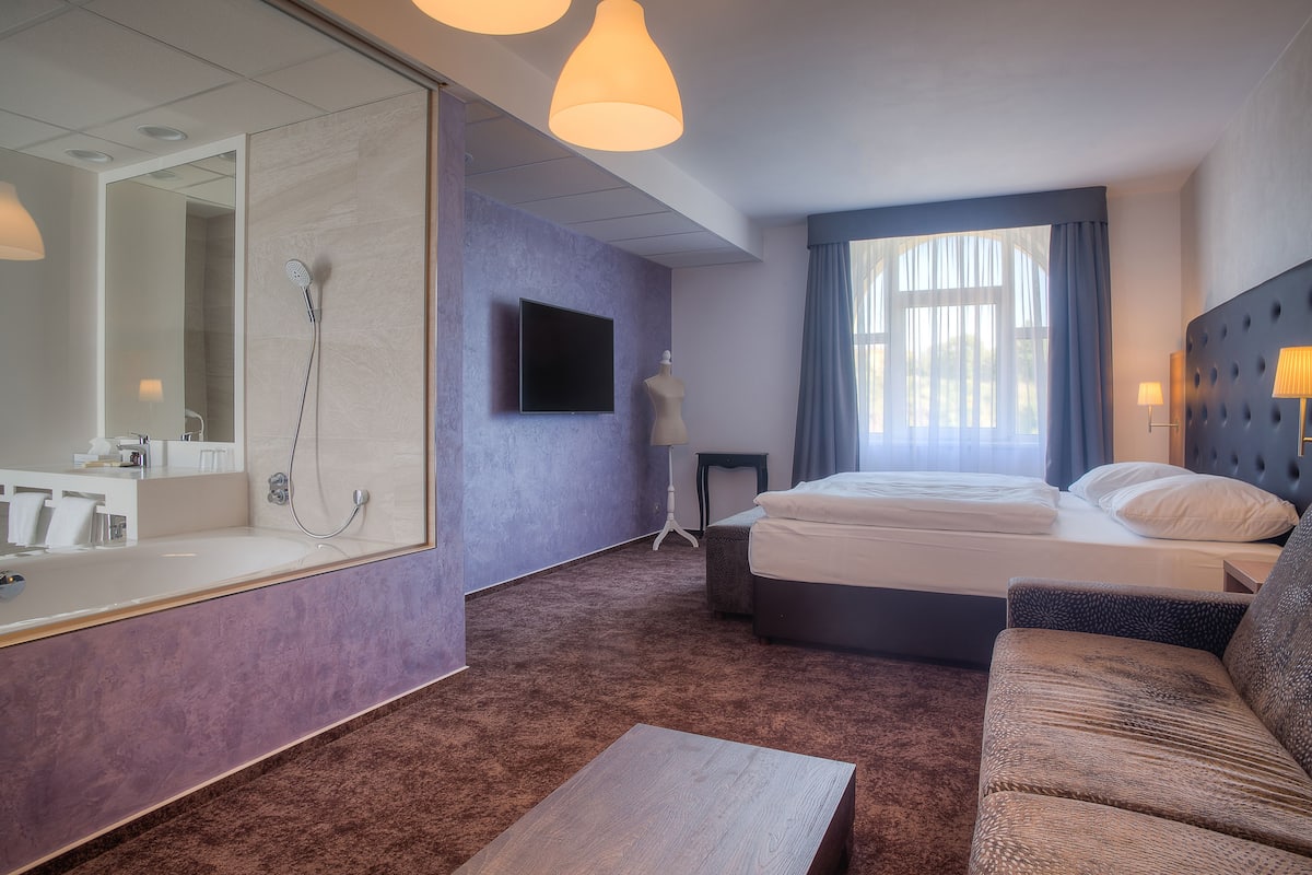 A modern hotel room with a large mirror, a bed, a sofa, and a television.