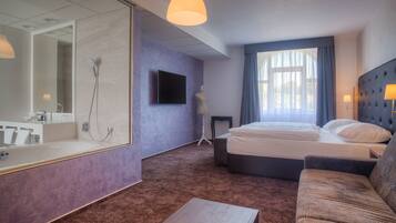 A modern hotel room with a large mirror, a bed, a sofa, and a television.