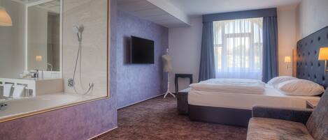 A modern hotel room with a large mirror, a bed, a sofa, and a television.
