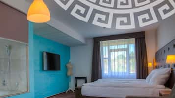 Habitación de hotel con una cama grande, televisión, ducha y vistas al exterior.