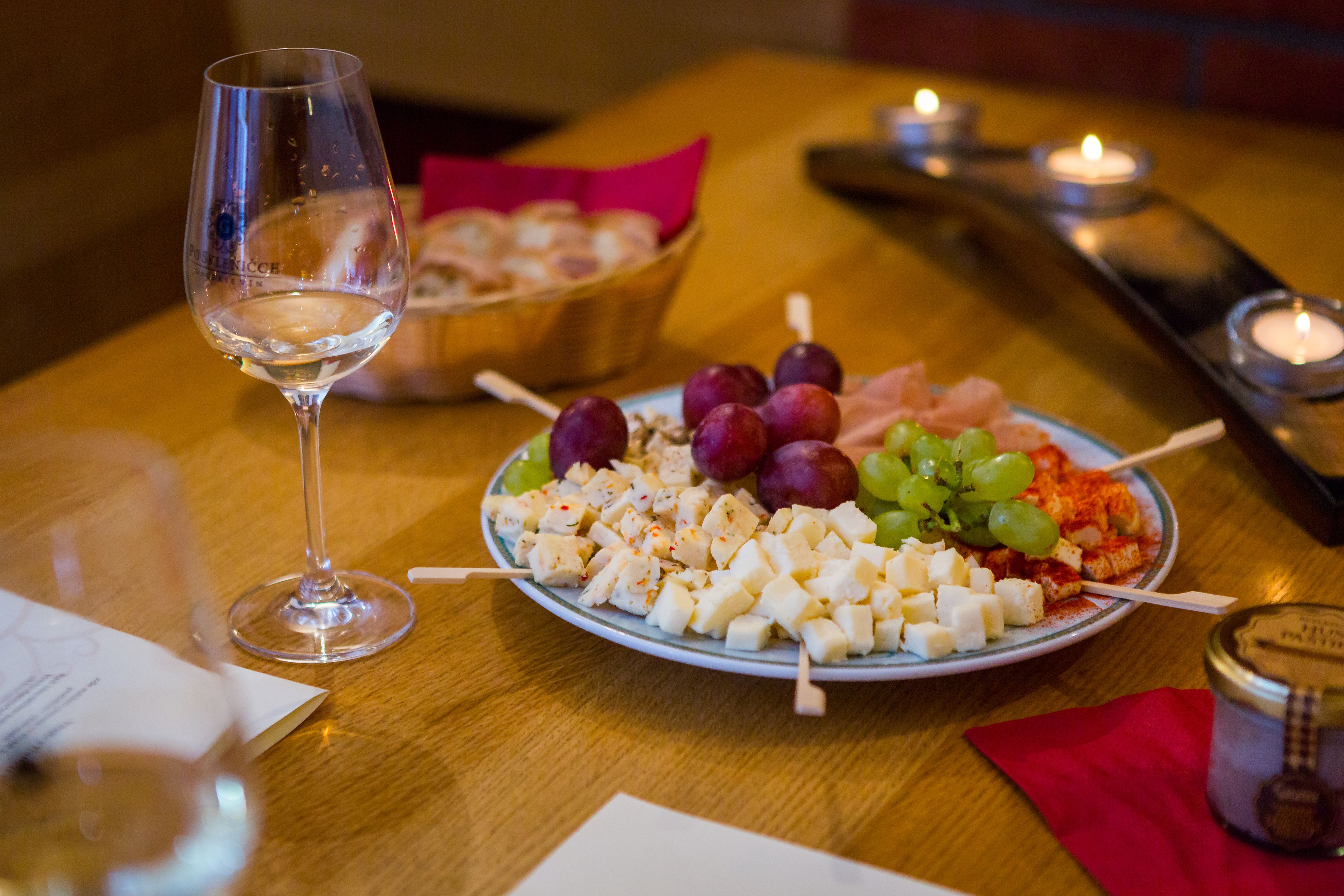 Et spisebord med en tallerken med ost og druer, et glas hvidvin og et stearinlys.