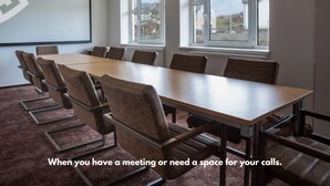 Un salón de conferencias con una larga mesa y sillas, ventanas amplias y una pantalla de proyector.
