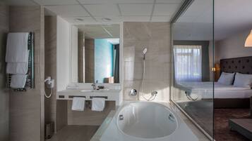 A modern hotel bathroom with a large bathtub, a vanity with a mirror, and a shower.