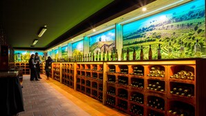 Una bodega con hileras de botellas de vino y un mural de un viñedo en la pared.