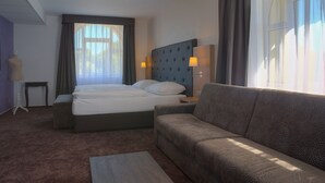 Habitación de hotel con una cama grande, un sofá, una mesita y una lámpara.