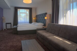 Habitación de hotel con una cama grande, un sofá, una mesita y una lámpara.
