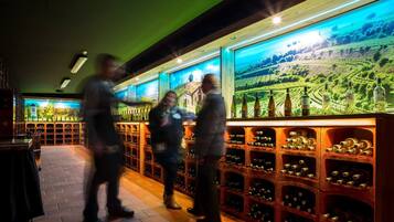 A wine cellar with wooden racks filled with bottles, a large mural of a vineyard, and a brick floor.