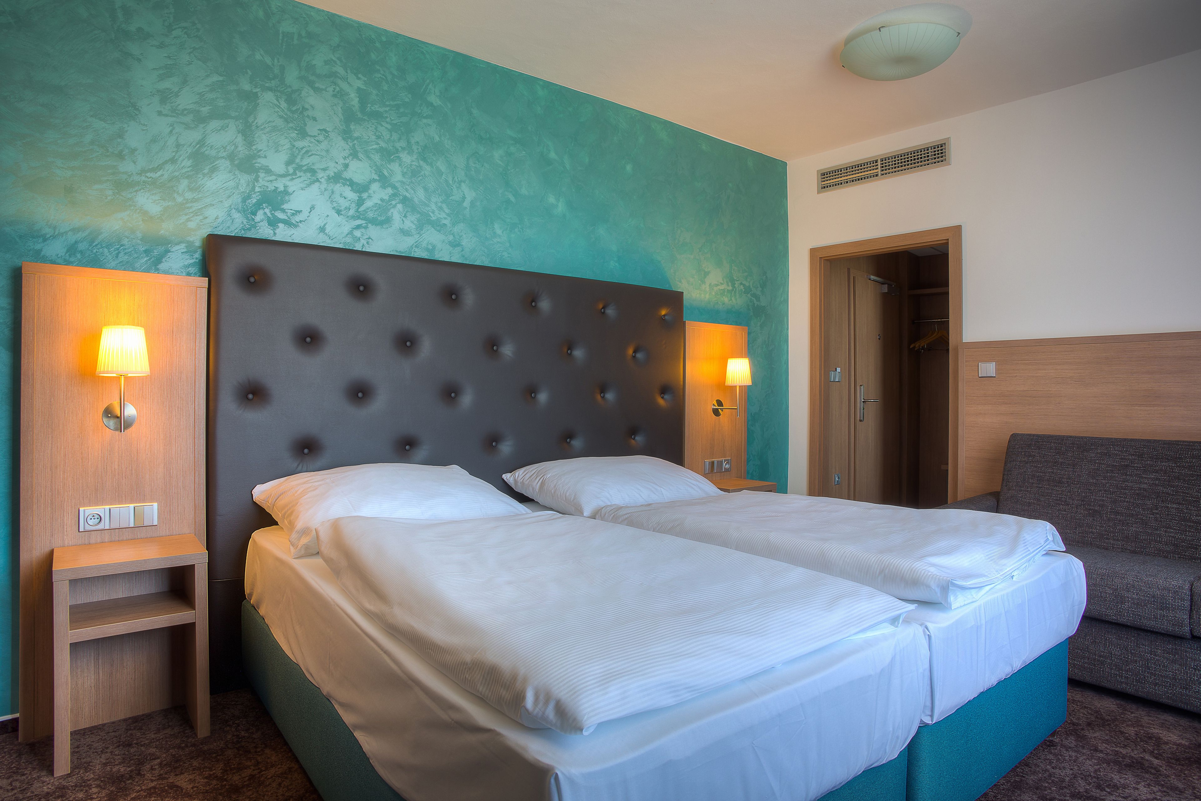 A hotel room with a double bed, two bedside tables, a nightstand, a sofa, and a door leading to a bathroom.
