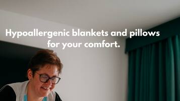 A person adjusting a bed in a hotel room with hypoallergenic blankets and pillows.