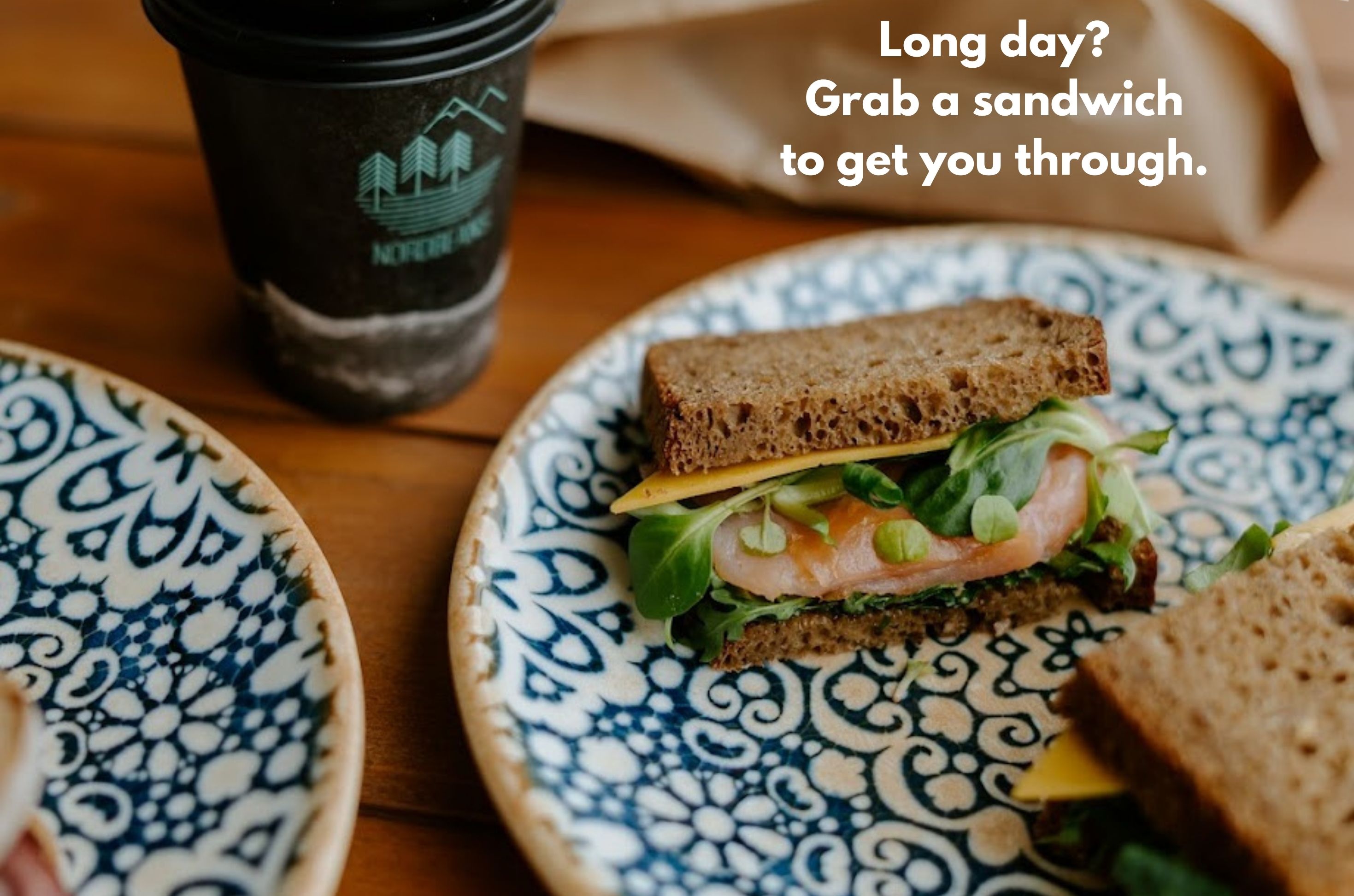 A sandwich on a patterned plate with a coffee cup in the background.