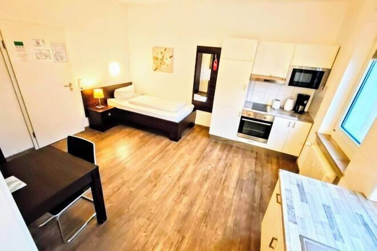 Une chambre de taille modeste comprenant un lit, une petite table, un bureau, un coin cuisine et un téléviseur.