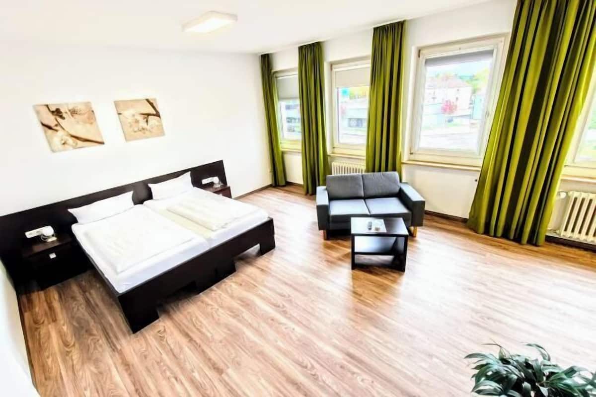 Une chambre d’hôtel avec un lit, un canapé, une table basse et une plante en pot.
