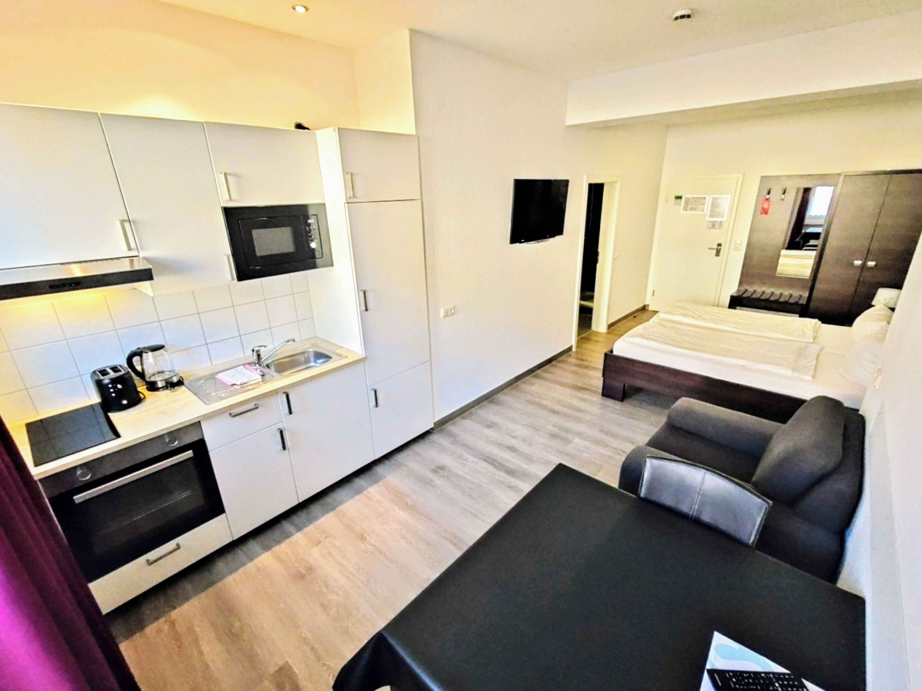 Una habitación de hotel compacta con kitchenette, una cama, un sofá y un escritorio.