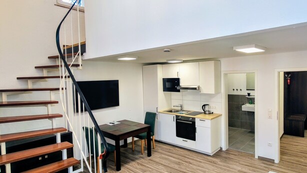 Un appartement moderne doté d’un escalier menant à une chambre en mezzanine, d’une cuisine avec des meubles blancs et d’un espace de vie comprenant un canapé et une table basse.