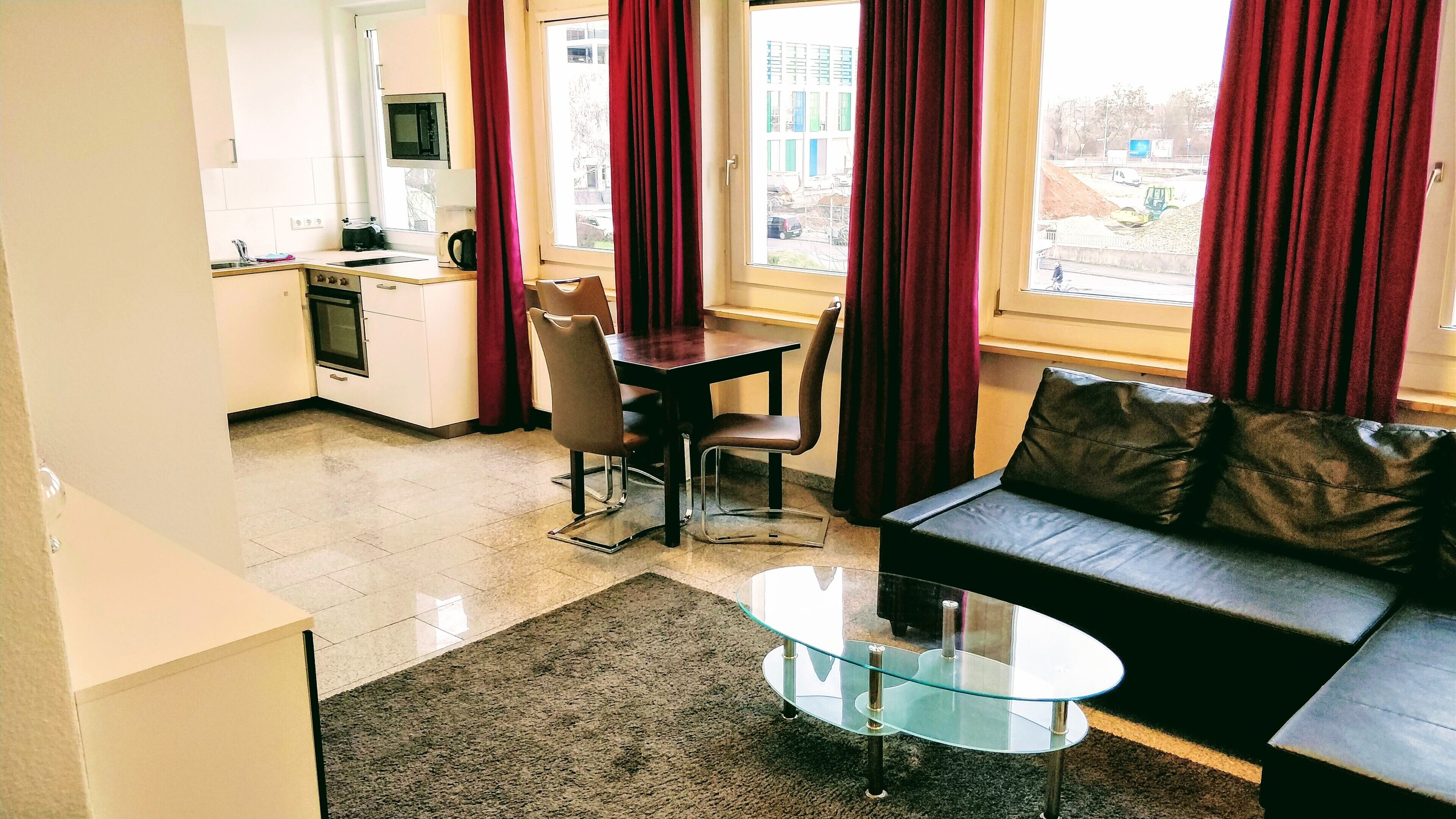 Un espacio habitable compacto con un sofá, una mesa de centro de vidrio, una mesa de comedor con sillas, una zona de cocina con microondas y vistas al exterior a través de amplios ventanales.