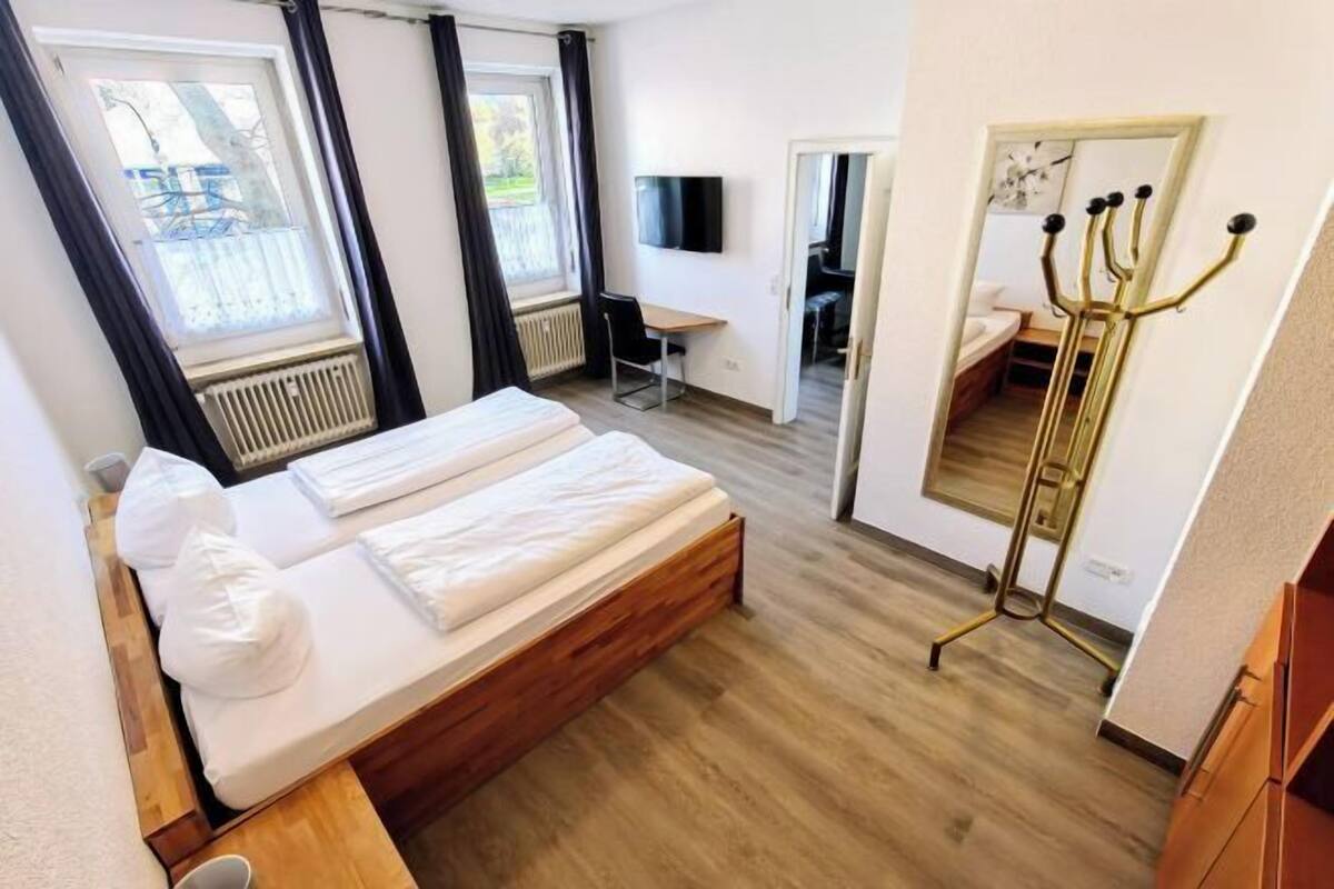 Une chambre d’hôtel équipée d’un lit, d’un bureau, d’une chaise, d’une télévision, d’un miroir et d’une fenêtre avec des rideaux.
