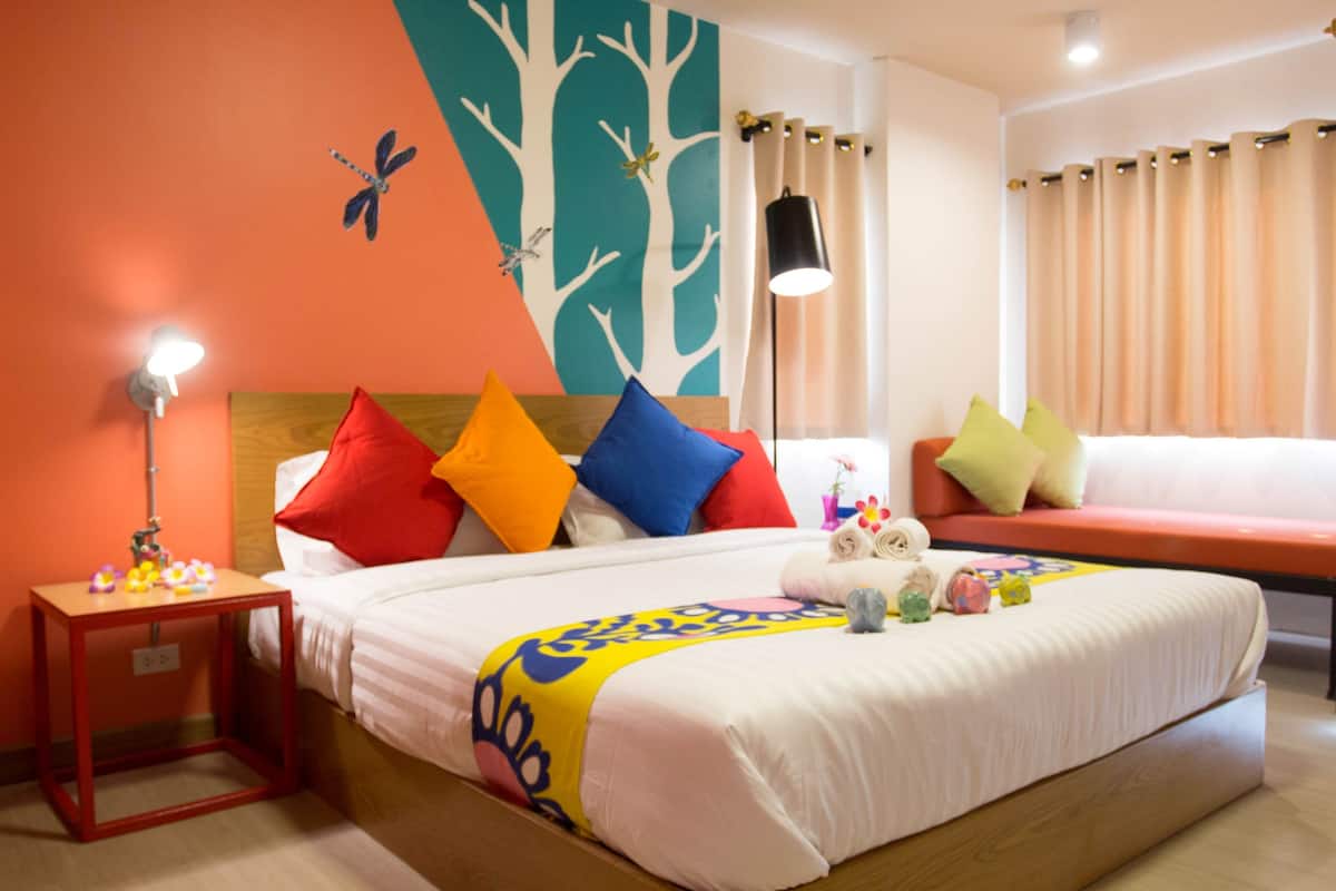 A hotel room with a bed, a nightstand, a lamp, and a wall with a tree and butterfly mural.
