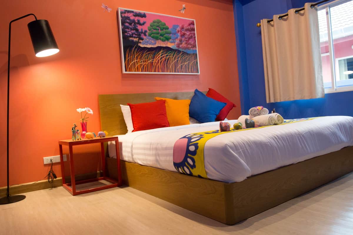 A bedroom with a bed, a nightstand, a lamp, a painting, and a window with curtains.