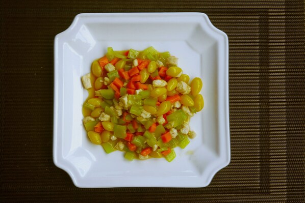 A white plate with a colorful vegetable salad on a dark textured surface. - The Hotel Nova (Mandalay)