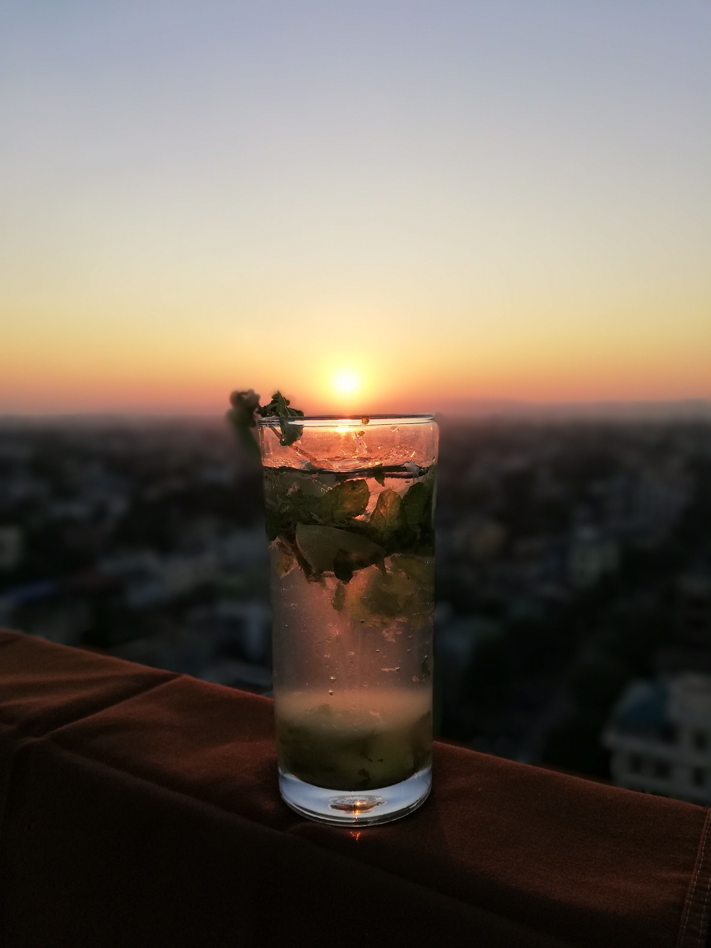 Un vaso alto con una bebida, sobre una superficie con vista al atardecer.