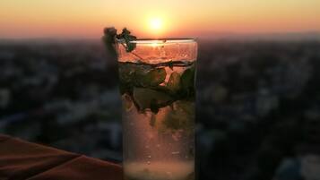Un vaso alto con una bebida, sobre una superficie con vista al atardecer.