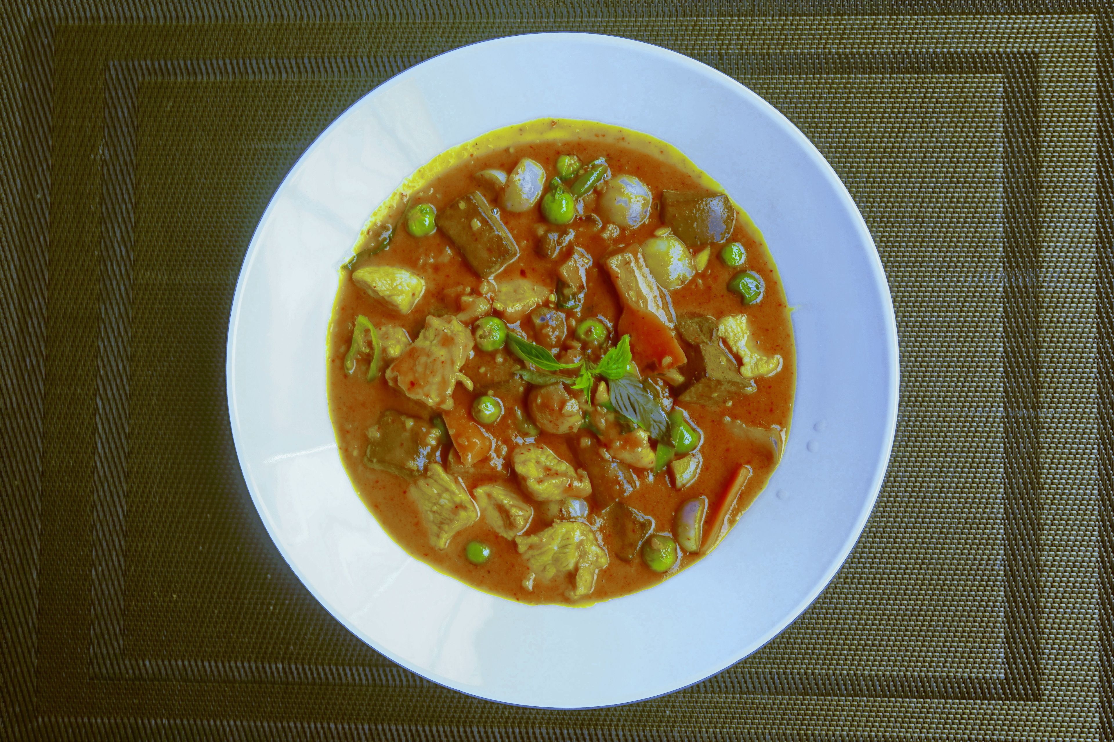 A bowl of curry with vegetables and meat on a white plate.