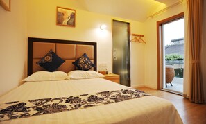 Une chambre d’hôtel avec un lit, une table de chevet, un tableau, une porte et une vue sur l’extérieur.
