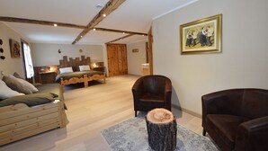 A cozy room with a wooden bed, a leather armchair, and a rustic wooden stool. - Albergo Herbetet (Cogne)