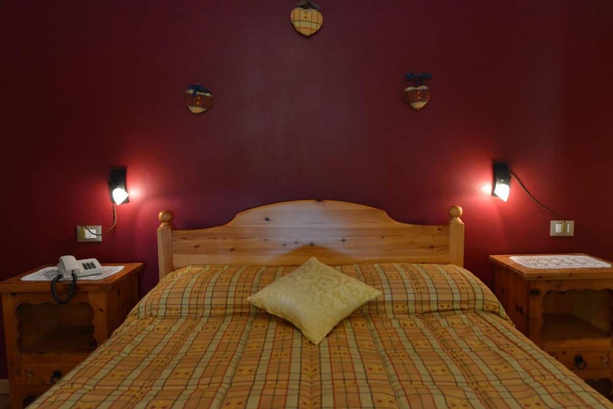 A room with a wooden bed, two bedside tables, a telephone, and wall-mounted lamps.