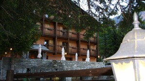 A multi-story building with balconies, stone walls, and outdoor umbrellas. - Albergo Herbetet (Cogne)