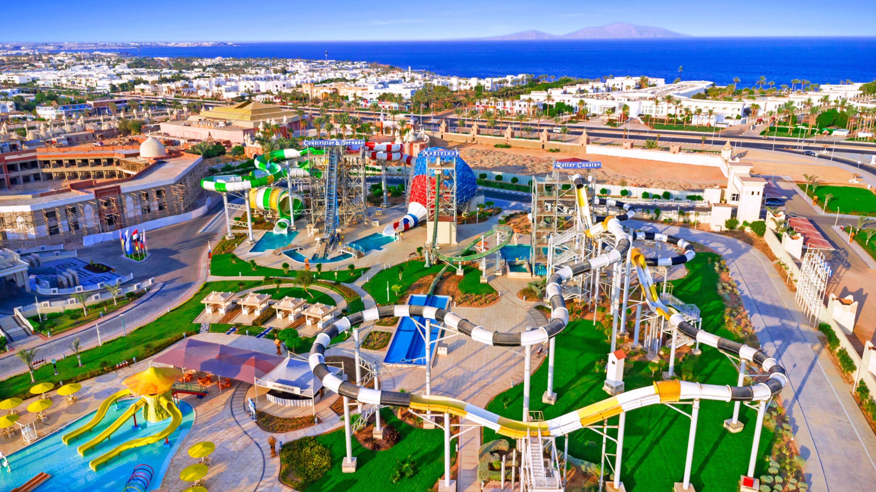 Parque acuático con toboganes y piscinas, rodeado de edificios y vistas al mar.