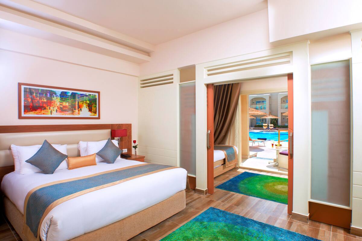 Ein Hotelzimmer mit einem großen Bett, einem Bild an der Wand und Blick auf einen Poolbereich.