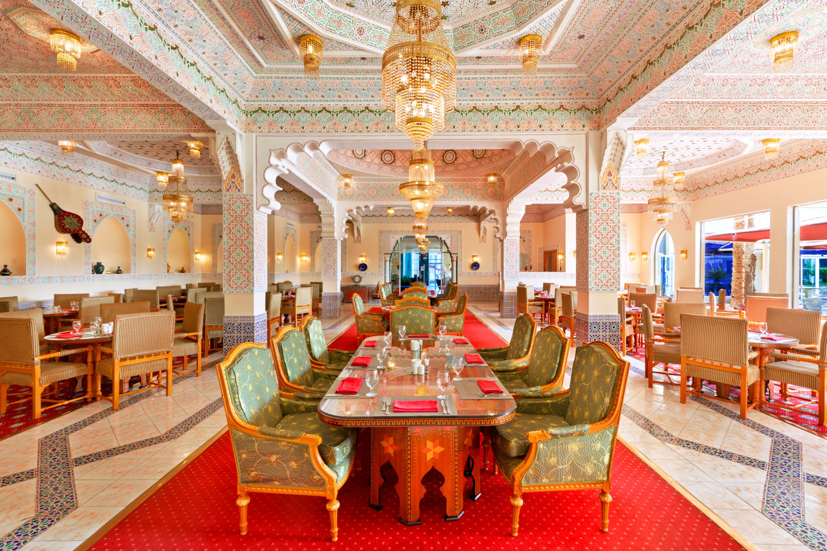 A spacious dining area with ornate chandeliers, patterned walls, and traditional seating.