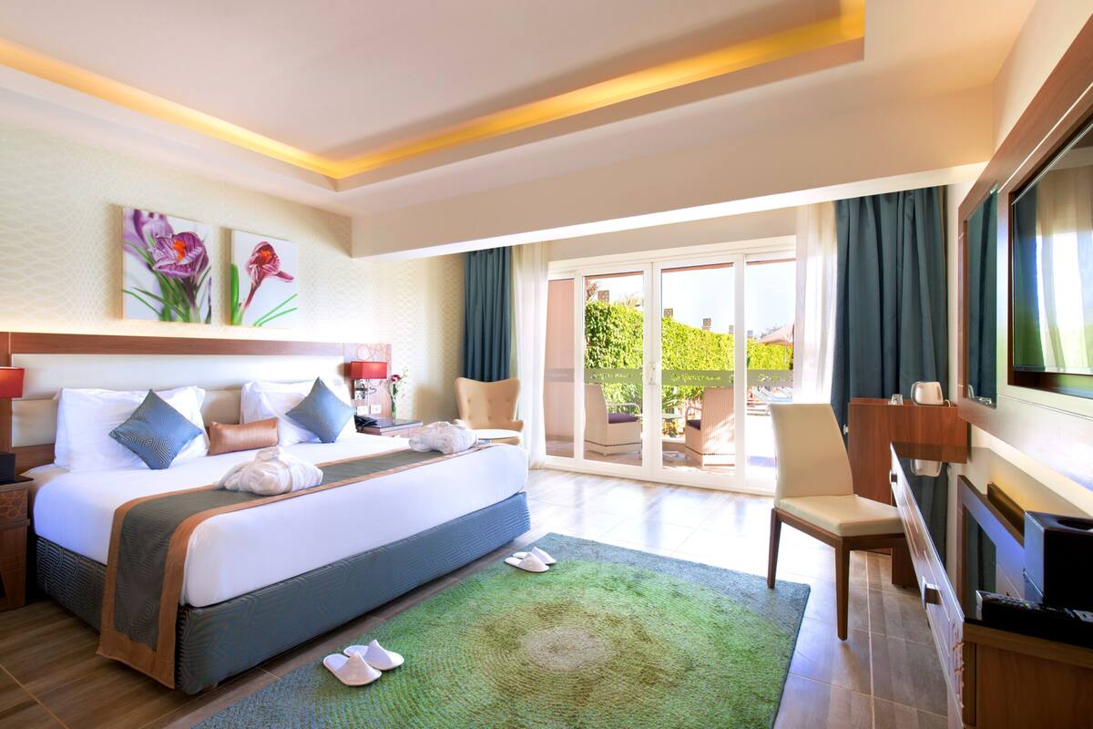 Ein Hotelzimmer mit einem großen Bett, einem Fernseher, einem Schreibtisch und Blick ins Freie.