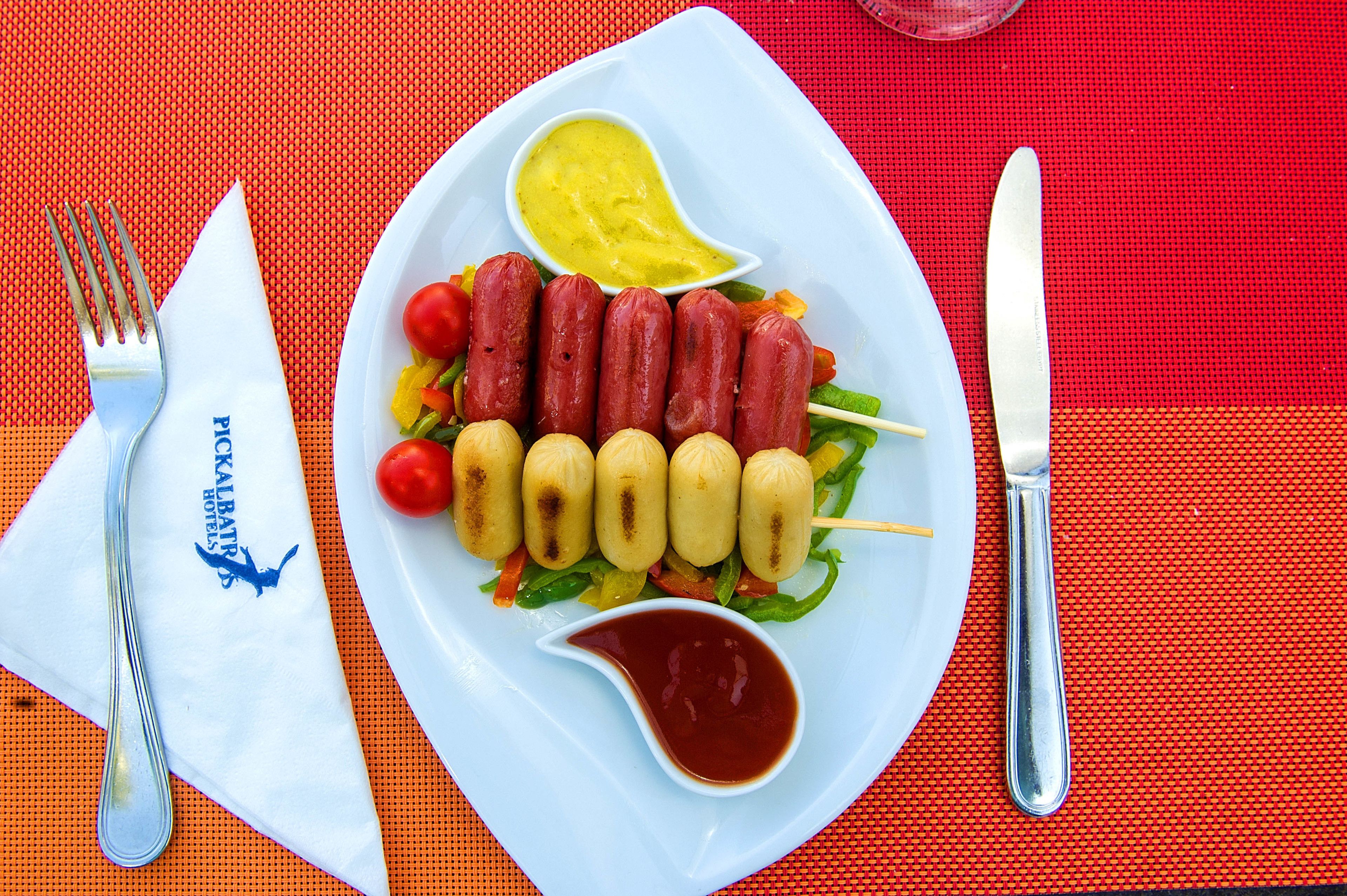 A plate with skewers of meat and vegetables, a small bowl of sauce, and a napkin with a logo.