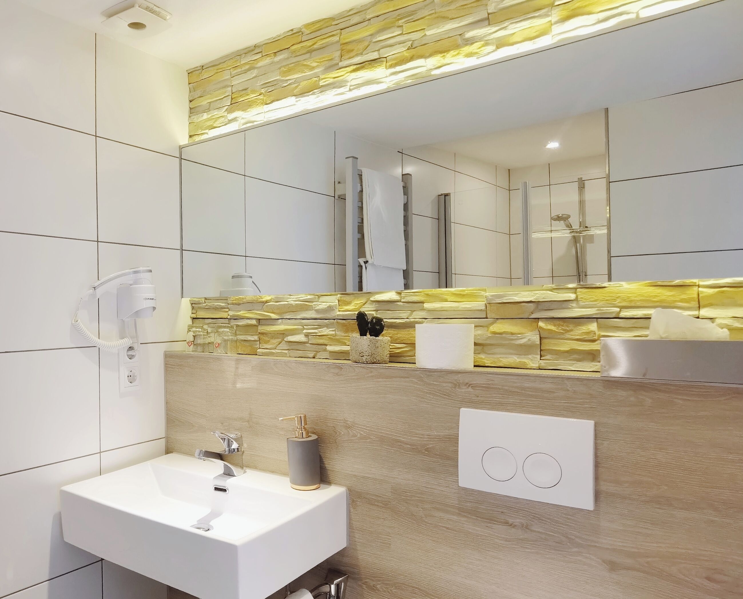 A modern bathroom with a white sink, a stone backsplash, a mirror, and a shower.