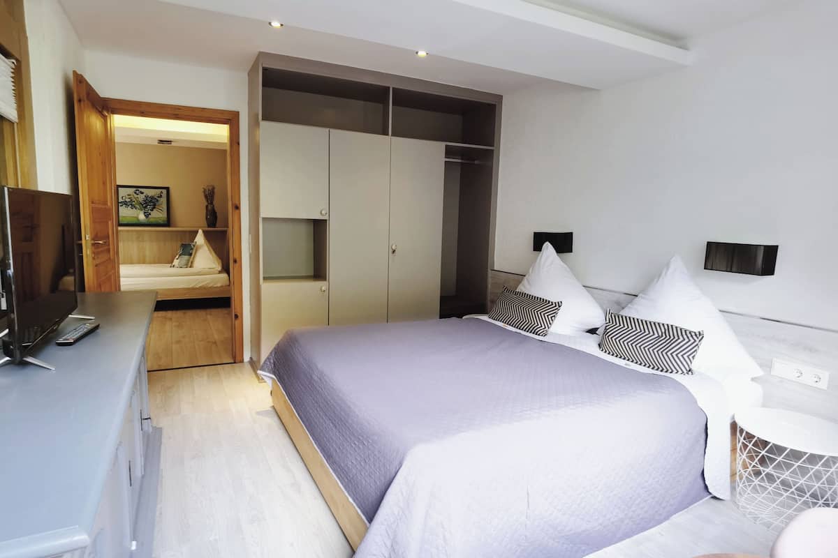 Un dormitorio moderno con una cama grande, un armario, un escritorio con una computadora y un televisor.