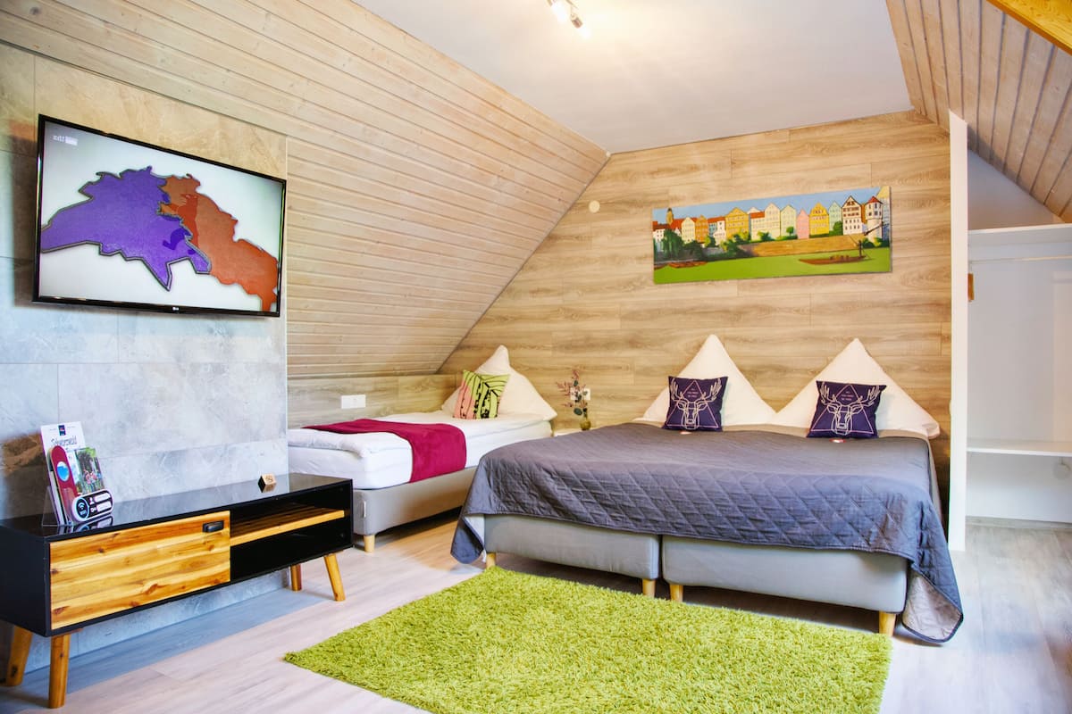Un dormitorio con cama, televisión, cabecero de madera y un cuadro en la pared.