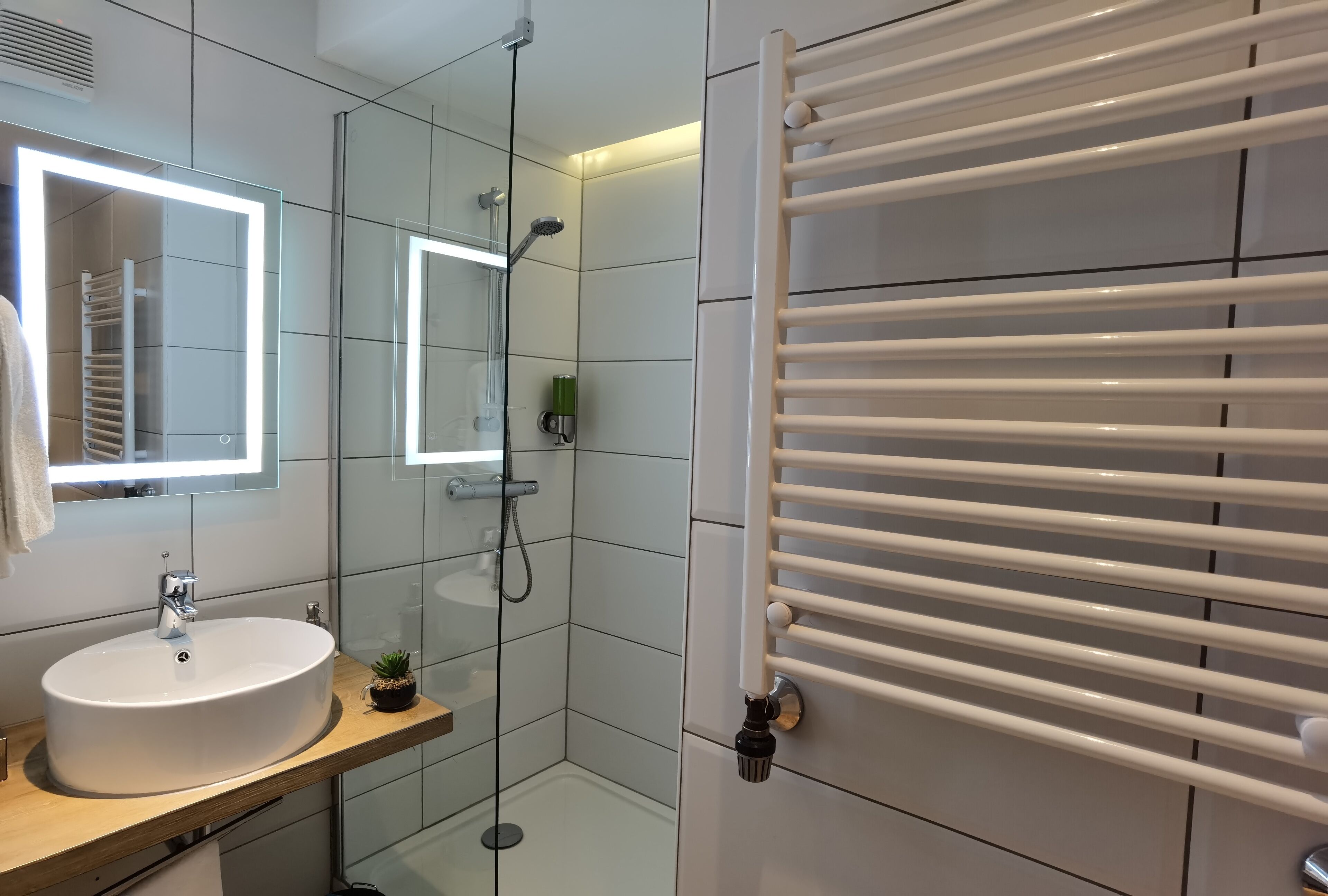 A modern bathroom with a large mirror, a white sink, a glass shower enclosure, and a towel rack.